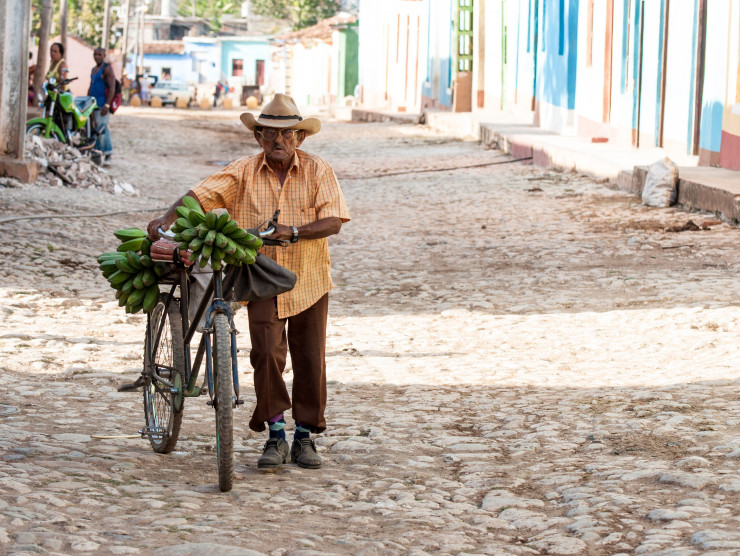 Auf einer kopfsteingepflasterten Straße schiebt ein Kubaner sein Rad mit Bananen entlang